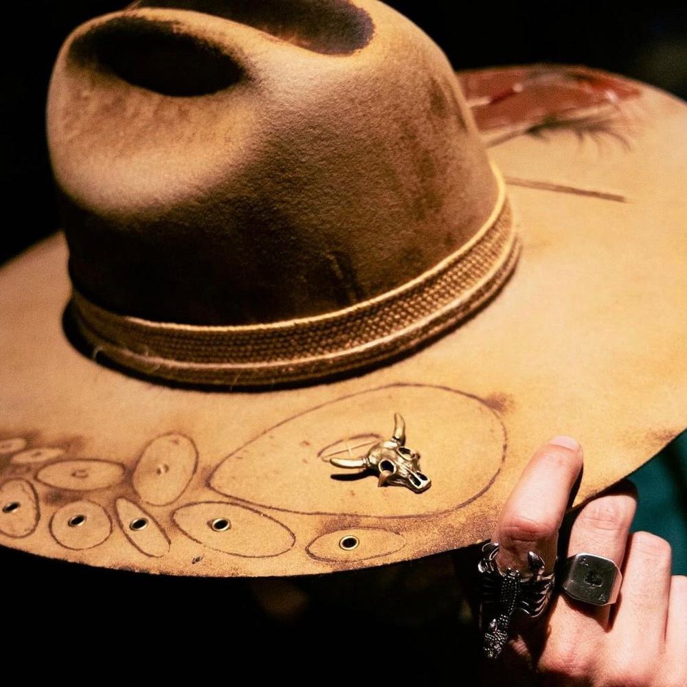 Yellow Felt hat, tilted on one side by a hand  with a scorpion ring. the face is not visible the light is on the hat a bit yellowish