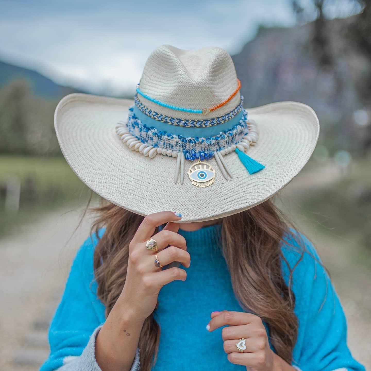 Woman wearing a white hat with many laces at the crown displaying details in a marine blue tone and orange beads