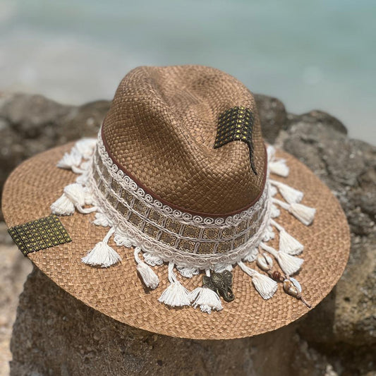 Woven brown hat, with several intricate and colorful details at the base of the crown and white string falling