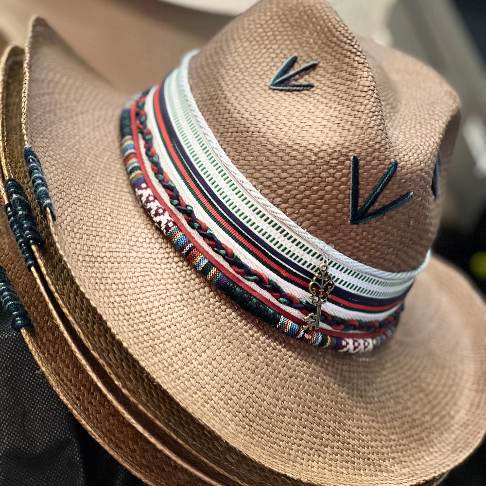 Woven brown hat, with several intricate and colorful details at the base of the crown and string markings at the top