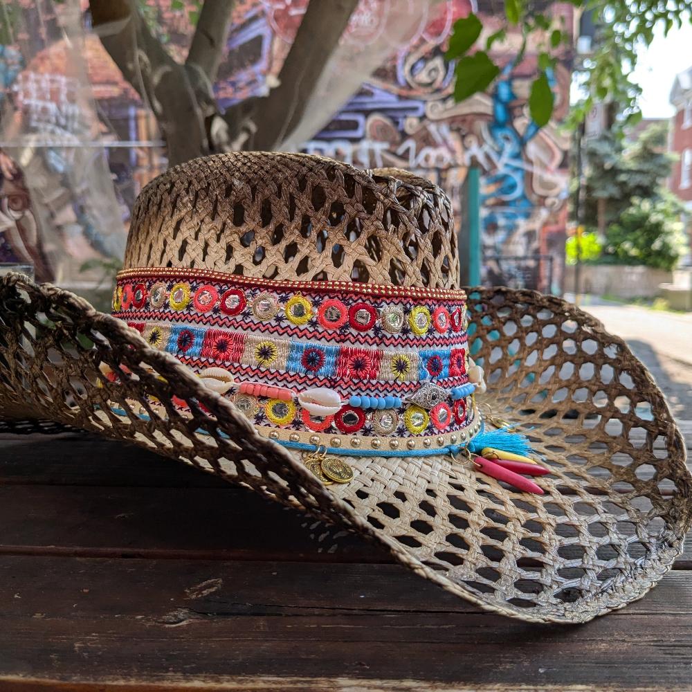 Woven white hat, with several intricate and colorful details at the base of the crown modeled in a western style