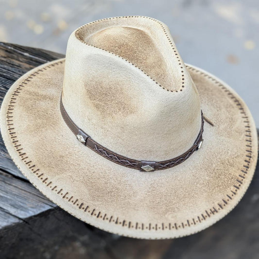 Beige felt hat placed on a wooden bench; there is a leather lace at the base of the crown and markings making the hat look ruged